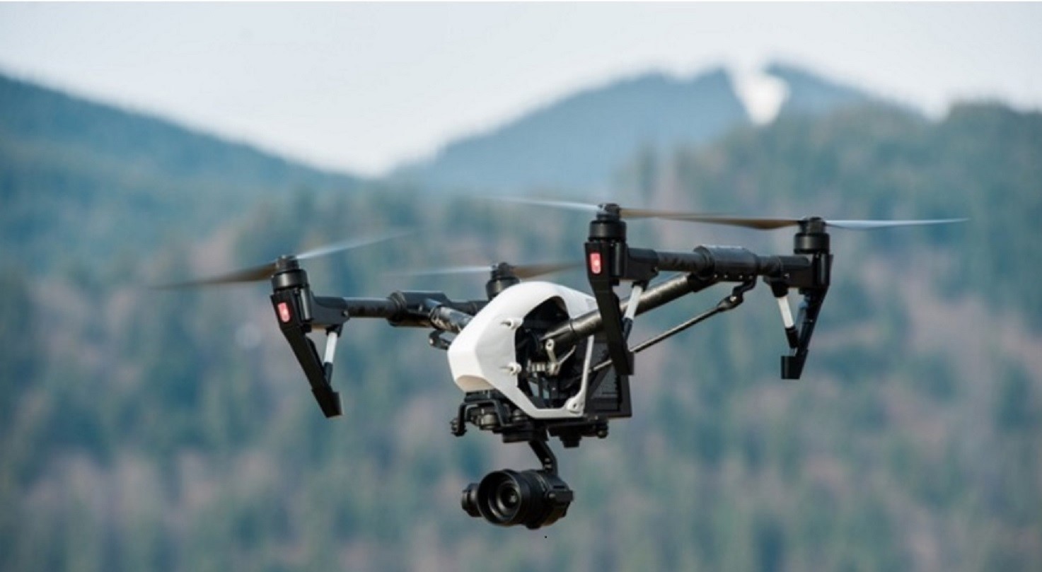 Image of a drone flying in a mountainous landscape covered with forest.